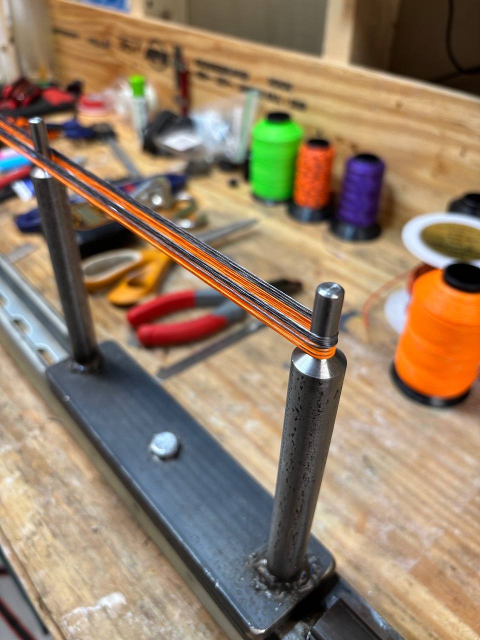 A close view of the orange-and-black strands laid cleanly around the main jig post during the initial layup.