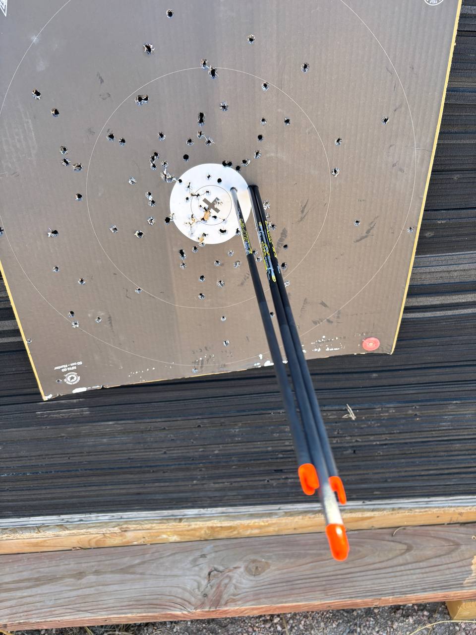 Two bare shaft arrows with orange nocks grouped tight in the center of a cardboard hunter target