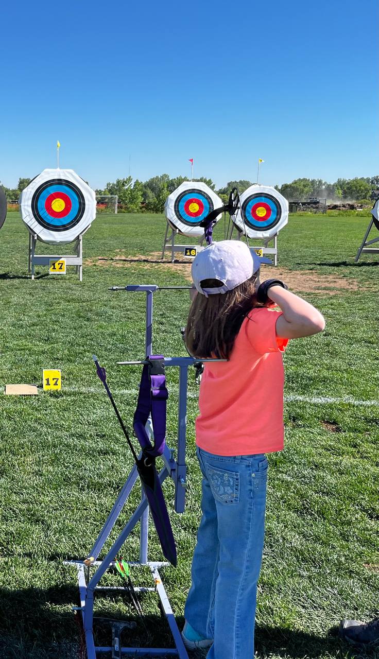 PARA VI archery tactile sight in use at an outdoor archery range — a compound archer wearing a blindfold draws at full draw with the tactile reference stand positioned in front